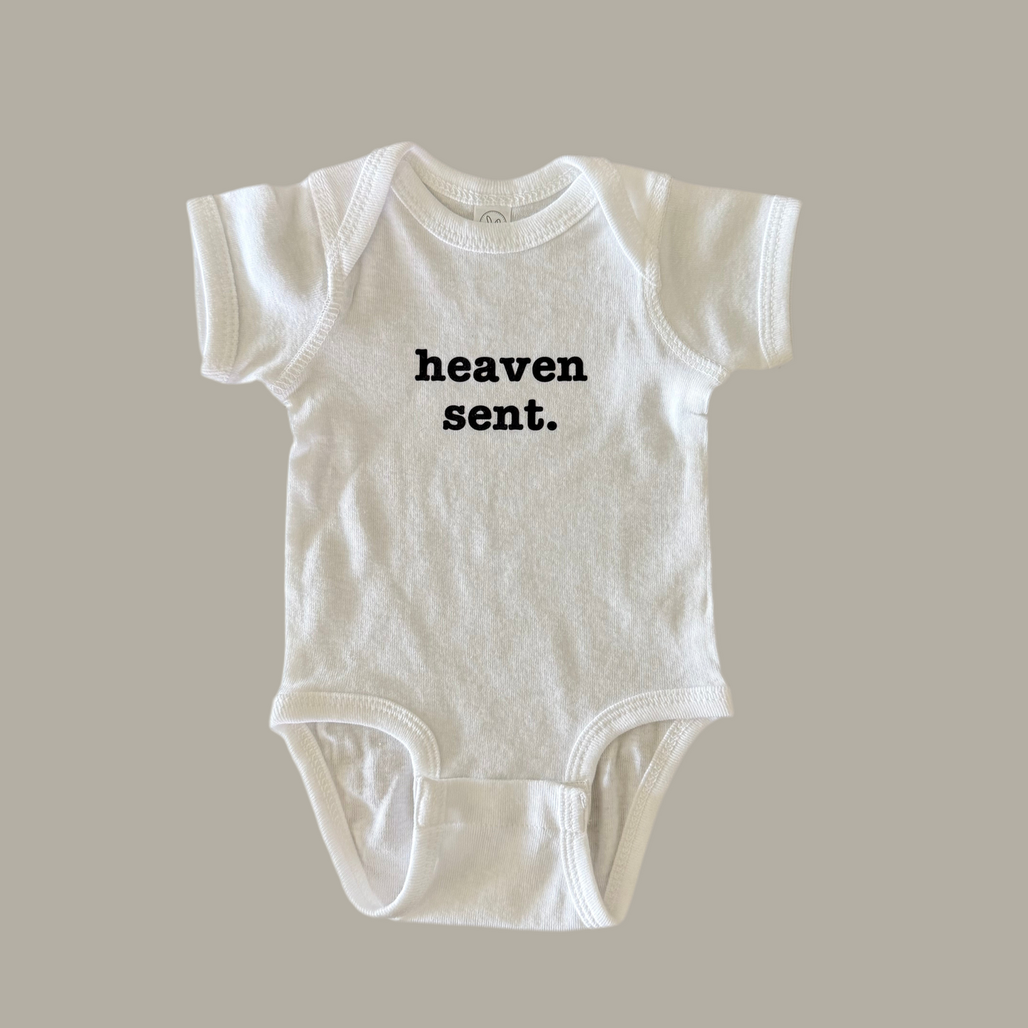 White baby onesie with 'heaven sent.' text on it