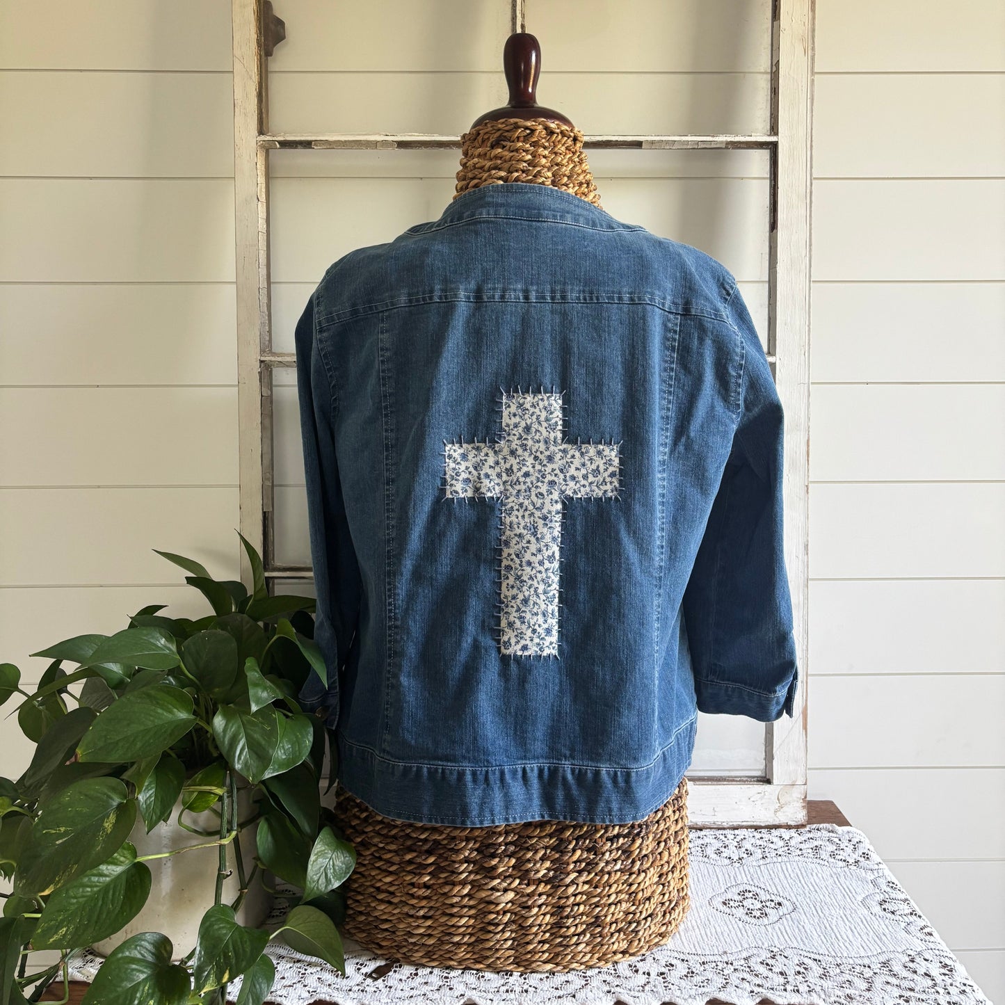 A size 16, dark wash, denim jacket with embroidery and jewels along the collar and a floral cross hand stitched into the back, displayed on a mannequin.