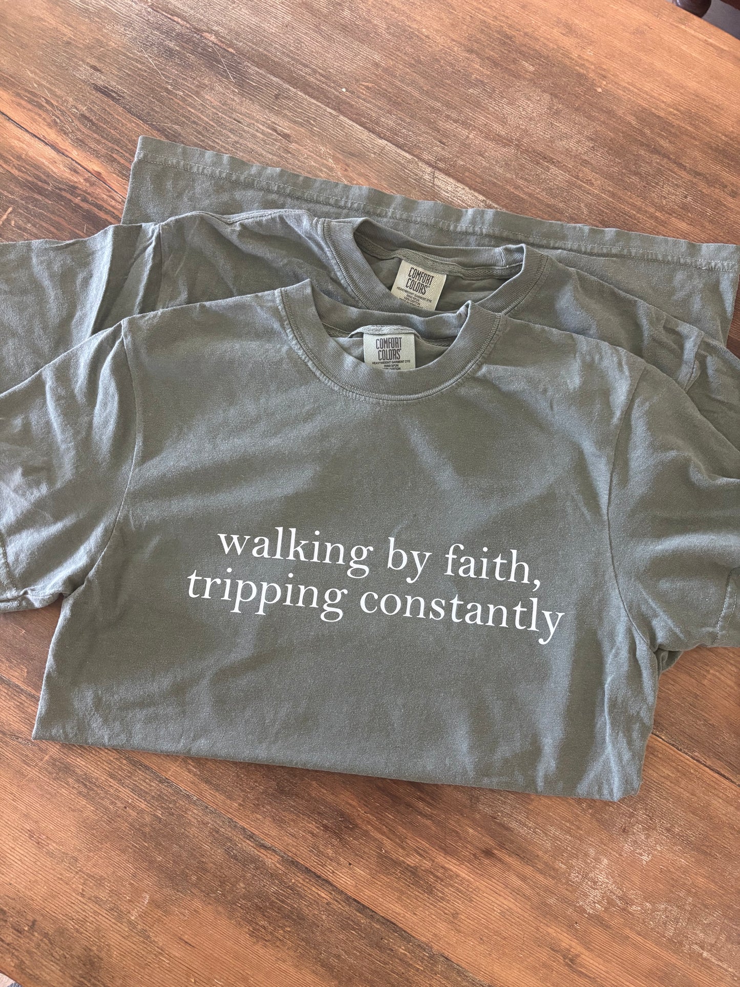 olive green shirt with the quote "walking by faith tripping constantly"