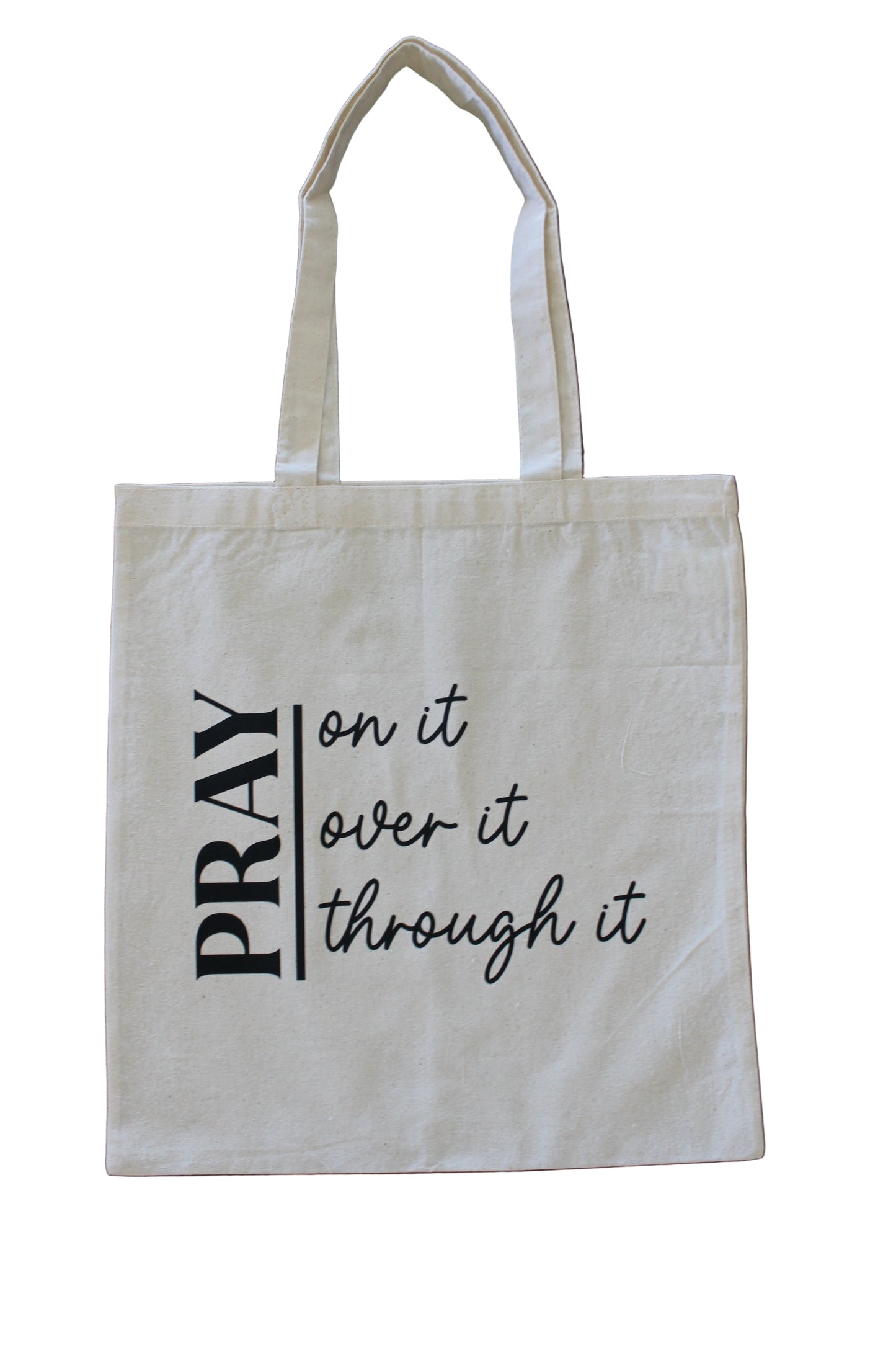 A canvas tote bag with a Christian design pray on it, over it, and pray through it