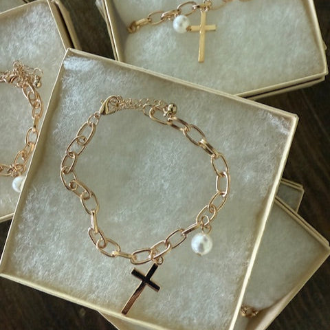 Gold chain bracelet with a cross charm in a jewelry box on a wooden surface